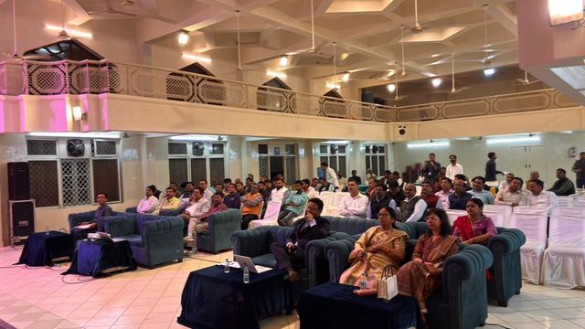 Community hall with a balcony above and attendees seated in rows facing the stage